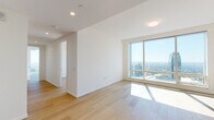 This single-floor high-rise residence offers a sleek, contemporary design defined by clean lines, crisp white walls, and light-toned hardwood flooring that runs throughout the open living areas. Expansive floor-to-ceiling windows wrap around the space, flooding every room with natural light and framing breathtaking panoramic city skyline views that underscore the elevated position of this residence.

The open-plan living and dining area is generously proportioned, with a bright, airy atmosphere enhanced by recessed and flush-mount ceiling lighting. A corner section of wraparound glazing creates a striking vantage point, offering unobstructed sightlines across the urban landscape in multiple directions.

The kitchen is outfitted with rich walnut cabinetry complemented by high-gloss taupe upper cabinets and a clean white countertop. A gas cooktop, built-in double wall ovens, and an integrated refrigerator provide a full suite of premium appliances, while under-cabinet lighting adds a refined finishing touch.

The bathroom showcases a spa-inspired design with full marble-slab wall and floor tiling featuring elegant veining. A deep soaking tub sits beneath a glass panel with a handheld shower, while a separate walk-in shower, a wall-mounted toilet, and a floating walnut vanity with an illuminated mirror complete the sophisticated and functional layout.