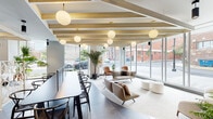 Located at 517 N Shipley Street in the heart of Wilmington, Delaware, this thoughtfully designed amenity floor offers a refined blend of modern architecture and functional communal spaces. The welcoming lobby entrance features striking large-format marble-look tile flooring, a curved accent wall with vertical slat detailing, lush indoor greenery, and a convenient coffee and beverage station. The expansive lounge area is defined by exposed wood beam ceilings, globe pendant lighting with brass accents, and floor-to-ceiling windows that bathe the space in natural light while offering open views of the surrounding streetscape. Seating areas include a mix of sofas, lounge chairs, and a long communal dining table ideal for gathering. A dramatic steel-clad fireplace wall with a linear hearth and mounted television serves as a striking focal point in the lounge's cozy corner. The fitness center is generously sized and fully equipped with treadmills, ellipticals, rowing machines, and cycling equipment, complemented by floor-to-ceiling mirrors and direct access to a landscaped outdoor terrace with string lighting and seating. Adjacent to the fitness area, a glass-partitioned game room with billiards adds a social dimension to the amenity offering. Together, these spaces create a cohesive and vibrant environment suited for both relaxation and active living.