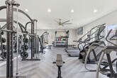Located at 7450 Northrop Dr in Riverside, California, this fitness center offers a thoughtfully designed workout space with a comprehensive range of exercise equipment. The single-floor facility features stylish herringbone-patterned flooring throughout, crisp white walls, and recessed lighting complemented by a ceiling fan that keeps the space well-ventilated and comfortable.

The cardio zone is well-stocked with multiple Matrix treadmills, stair climbers, and elliptical machines, all positioned to take advantage of the natural light flowing in through the windows. Wall-mounted flat-screen TVs provide entertainment during workouts, while a large, vibrant abstract wall mural adds an artistic focal point to the space.

The strength training area is equally impressive, featuring a Matrix cable/functional trainer machine, a rack loaded with weight plates, adjustable benches, and a dedicated free weights station. The free weights section includes an organized rack of dumbbells, kettlebells, medicine balls, and resistance bands, catering to a wide variety of training styles.

Floor-to-ceiling mirrors in the strength area enhance the sense of space and allow users to monitor their form. The facility is accessible via multiple entry points and maintains a clean, modern aesthetic that makes it an inviting environment for residents seeking a convenient and fully equipped place to exercise.