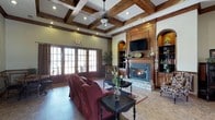 Located at 755 CL Tart Circle in Fayetteville, NC, this single-story space exudes warmth and classic elegance through its thoughtfully designed interior. The living area serves as the centerpiece of the space, immediately drawing attention to its dramatic coffered ceiling adorned with rich, dark wood beams that add architectural depth and visual interest overhead. Recessed lighting is integrated throughout the ceiling, complementing the natural light that pours in through a row of tall French doors along one wall, offering a bright and welcoming ambiance.

A stone-surround fireplace anchors one wall, flanked by custom wood built-ins featuring arched alcoves and open shelving — ideal for displaying décor and housing media equipment, including a mounted flat-screen television above the mantle. The warm tones of the wood millwork throughout create a cohesive, traditionally styled interior. The flooring features large-format tile, adding a polished, durable surface that ties the space together. Comfortable seating, decorative rugs, and accent tables complete the inviting, well-appointed atmosphere of this refined space.