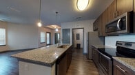 Located at 2509 Cattlemen Rd in Sarasota, Florida, this single-floor unit offers a thoughtfully designed open-concept layout with contemporary finishes throughout. The kitchen is a standout feature, showcasing rich dark wood cabinetry, granite countertops, a large central island with an undermount sink and pendant lighting, a white subway tile backsplash, and a full suite of stainless steel appliances including a range, over-the-range microwave, dishwasher, and refrigerator. Wood-look flooring flows through the kitchen and into the generous living area, which is bathed in natural light from large windows with blinds and includes a ceiling fan overhead. The open floor plan connects the kitchen and living space seamlessly, creating an airy and functional environment. Bedrooms are carpeted for comfort, feature ceiling fans, and include walk-in closets with built-in shelving. The bathrooms are finished with granite-topped dark wood vanities, wood-look tile flooring, and tub-shower combinations with white subway tile surrounds and brushed nickel fixtures. The cohesive design palette of dark wood tones, granite surfaces, and neutral walls gives the entire space a clean, modern aesthetic.