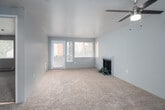 This single-floor residence offers a clean, neutral aesthetic throughout, making it a versatile and welcoming space. The living area is generously proportioned, featuring soft wall-to-wall carpeting in a warm beige tone that extends throughout the main living spaces. A tile-surround fireplace serves as a natural focal point, while a ceiling fan with a light fixture adds both function and character. Multiple windows, including a glass-panel exterior door, flood the room with natural light and provide views of the surrounding exterior. The open-concept layout connects the living area to the kitchen via a raised pass-through counter, offering a practical and social flow between spaces. The kitchen is well-appointed with white upper cabinetry, two-toned grey lower cabinets, light stone-look countertops, stainless steel appliances including a range and refrigerator, and tile flooring that adds durability and easy maintenance. A dedicated bedroom provides a quiet retreat, featuring carpeted flooring, a window with exterior views, and a baseboard heater. The full bathroom is finished with matching grey cabinetry, a granite-look countertop with an undermount sink, tile flooring, and a shower-tub combination. The overall design is cohesive and functional, with a neutral color palette that offers a calm and adaptable living environment.
