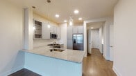 This thoughtfully designed single-floor residence offers a refined blend of modern finishes and functional living spaces. The kitchen serves as the heart of the home, showcasing a large central island topped with speckled granite and an undermount sink illuminated by elegant glass pendant lights. Soft gray shaker-style cabinetry lines the walls, complemented by a classic white tile backsplash and a full suite of stainless steel appliances, including a gas range, over-the-range microwave, and a French door refrigerator. Warm hardwood flooring flows throughout the main living and kitchen areas, adding depth and character to the space.

The primary bathroom is a standout feature, offering a dual-sink vanity with granite countertops, gray cabinetry, a large framed mirror, and a glass-enclosed walk-in shower with subway tile surround. A spacious walk-in closet is conveniently accessible from the bathroom.

The bedrooms are carpeted for comfort and feature tray ceilings with ceiling fans, large windows that frame expansive city and treetop views, and an abundance of natural light. Additional rooms with hardwood flooring provide flexible space for a den, office, or guest room. Throughout, the design maintains a clean, neutral palette with crisp white millwork and recessed lighting, creating a cohesive and welcoming atmosphere.