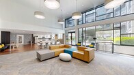 Located at 1250 E Burnside St in Portland's vibrant Lower Burnside neighborhood, this generously sized amenity floor offers a well-rounded collection of shared spaces designed for comfort, recreation, and community. The layout spans a substantial footprint, encompassing a fitness center, two distinct living and lounge areas, a full communal kitchen, and a connecting hallway.

The fitness center is well-appointed with hardwood-style flooring, large wall mirrors, and a comprehensive selection of cardio and strength equipment, including treadmills, an elliptical, cable machines, free weights, and stability accessories — all illuminated by sleek linear LED lighting.

The living and lounge areas offer distinct atmospheres. One features floor-to-ceiling grid windows that flood the space with natural light and offer views of a lush interior courtyard, complemented by modern furnishings and light patterned carpet. The other serves as a game room with two billiards tables, a wall-mounted television, accent lighting, and a mix of seating and high-top bar areas — ideal for social gatherings.

The communal kitchen is modern and well-equipped, showcasing white cabinetry, quartz countertops, stainless steel appliances, a gas cooktop island with bar seating, and pendant lighting throughout.

The hallway connects each area with a polished aesthetic, featuring bold striped flooring in mixed wood tones, dark wood paneling, and recessed lighting, establishing a cohesive and contemporary design throughout the entire floor.