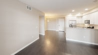 This single-floor residence is thoughtfully designed with a consistent warm neutral color palette and quality finishes throughout. The open-concept living and dining area is anchored by rich, dark hardwood flooring that extends through the main living spaces, complemented by neutral beige walls and recessed lighting. A pendant light fixture adds a decorative touch above the transition toward the entryway.

The kitchen is well-equipped with white shaker-style cabinetry reaching toward the ceiling, granite countertops, a breakfast bar peninsula, and a full suite of stainless steel appliances including a gas range, built-in microwave, and French door refrigerator with an in-door ice and water dispenser.

The bedrooms feature plush carpeting and windows with blinds that allow natural light and exterior views. A dedicated in-unit laundry closet houses a full-sized washer and dryer with overhead shelving for added storage.

Two bathrooms serve the unit: one with a soaking tub and shower combination, and a larger primary bathroom featuring a walk-in glass-enclosed shower, a vanity area, and dark hardwood-style flooring. A walk-in closet provides generous storage off the living area.