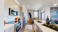 This well-appointed 2-bedroom, 2-bathroom residence in Erie, Colorado offers a thoughtfully designed single-floor layout that maximizes both function and style. The open-concept kitchen is a standout feature, showcasing sleek white cabinetry extending to the ceiling, stainless steel appliances including a French door refrigerator and range, and a large peninsula with a single-basin sink and bar seating — ideal for casual dining or entertaining. The adjacent dining area flows naturally from the kitchen and opens to an outdoor balcony through a glass door, filling the space with natural light. The living room features large windows framing neighborhood and mountain views, creating a bright and welcoming atmosphere. Both bedrooms are comfortably sized, with the primary offering ample closet space and a dedicated en-suite bathroom. The bathrooms are finished with white vanities, framed mirrors, and tile shower surrounds. Wood-style flooring runs throughout the main living areas, complemented by neutral tones that lend a clean, modern feel. A dedicated in-unit laundry closet houses a full-size front-loading washer and dryer with overhead shelving. Two closets provide additional storage throughout the home, making this residence as practical as it is attractive.