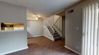 Located at 7901 South Yale Avenue in Tulsa, Oklahoma, this two-story residence offers a well-organized layout across two floors. The main level features rich hardwood-style flooring throughout the living and dining areas, with a ceiling fan overhead and a carpeted staircase with a white balustrade leading to the upper floor. A pass-through window connects the living area to the kitchen, providing an open sightline between the two spaces. Natural light filters in through vertical-blind-covered sliding glass doors, adding brightness to the living area. The galley-style kitchen is efficiently designed with dark wood cabinetry, light speckled countertops, a stainless steel sink, and black appliances including a refrigerator and microwave, complemented by light wood-style flooring. Upstairs, the carpeted bedrooms offer a comfortable retreat, with one room featuring a sliding glass door with vertical blinds and access to an outdoor area. The bathroom includes a wide vanity with dark wood cabinetry, speckled countertops, a large mirror, and a tiled shower-tub combination. Textured ceilings are consistent throughout the space, contributing to a classic residential aesthetic.