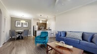 Located at 4891 Masch Branch Rd in Krum, TX, this single-story 2-bedroom, 2-bathroom home offers a thoughtfully designed open-concept layout. The living room features rich hardwood-style flooring, crown molding, a ceiling fan, and large windows with a glass door that invite abundant natural light and outdoor views. The space flows seamlessly into the kitchen and dining area, creating an ideal setting for daily living and entertaining.

The kitchen is well-equipped with stainless steel appliances, including a refrigerator, microwave, and range, complemented by dark cabinetry, granite-style countertops, and a peninsula with seating. Pendant lighting adds a polished touch overhead. The adjacent dining area provides an intimate setting with warm-toned walls and hardwood-style flooring.

The primary bedroom features plush carpeting, a window for natural light, and access to its own bathroom. The second bedroom, also carpeted, comfortably accommodates multiple beds and benefits from a large window. Both bathrooms are finished with dark cabinetry, granite-style countertops, large vanity mirrors, and wood-look tile flooring. A hallway connects all rooms efficiently, rounding out this functional and attractively finished home.