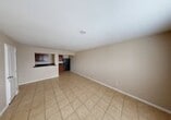 This single-floor residence offers a functional and straightforward layout across two bedrooms and two bathrooms. The open living area is finished with neutral-toned tile flooring and warm beige walls, creating a clean, understated ambiance throughout. The kitchen is accessible via a pass-through opening from the living space, featuring rich dark wood cabinetry, dark granite-style countertops, a black refrigerator, and a range — providing ample storage and workspace in a compact yet efficient layout. The primary bedroom offers a comfortable amount of space with matching tile flooring, neutral walls, and a ceiling vent for climate control. A second bedroom receives natural light through a window fitted with blinds, maintaining the same consistent palette found throughout the home. Both bathrooms are tiled and equipped with vanities featuring wood cabinetry and mirrors. One bathroom includes a soaking tub and a separate shower area, while the second features a walk-in shower and an overhead light bar above the vanity. A hallway connects the living areas to the bedrooms and bathrooms, contributing to an organized and efficient flow throughout the home. The consistent use of light tile, neutral walls, and white trim gives the entire space a cohesive, move-in-ready appearance.