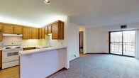 This single-floor residence offers a thoughtfully organized layout with a range of functional spaces. The kitchen is a standout feature, equipped with warm honey-toned oak cabinetry extending to the ceiling, light countertops, a double stainless steel sink, and white appliances including a refrigerator, electric range, and dishwasher. Light wood flooring adds warmth to the kitchen, which opens to the living area via a peninsula counter. The open living and dining area is generously sized, featuring neutral carpet, cream-toned walls, and a decorative chandelier that anchors the dining space. The layout flows seamlessly between rooms, creating an airy and connected feel. There are multiple carpeted bedrooms, each with ample closet space — notably, one bedroom features dual sliding-door closets offering extensive storage. Additional bedrooms include windows with exterior views and individual closets. The residence includes two bathrooms: a full bathroom with a tub/shower combination, tile flooring, vanity with under-sink storage, and a large mirror; and a second bathroom featuring a glass-enclosed walk-in shower, vanity, and tile flooring. Textured ceilings are present throughout, and consistent wood-toned trim ties the interior together cohesively.