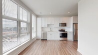 Located at 1350 W Fifth Ave in Columbus, OH, this efficiently designed one-bedroom, one-bathroom residence offers a clean, modern aesthetic throughout. The open-concept kitchen and living area serves as the heart of the unit, featuring white shaker cabinetry extending to the ceiling, a white subway tile backsplash, light countertops, and a full suite of stainless steel appliances including a refrigerator, electric range, built-in microwave, and dishwasher. Large windows flood the combined living and kitchen space with natural light and provide views of the surrounding neighborhood. Durable wood-look plank flooring runs throughout the entire unit, lending a cohesive and contemporary feel. The bedroom is a bright, calm retreat with its own window offering outdoor views and ample closet access. The bathroom features a white vanity with an undermount sink, clean white finishes, and matching wood-look flooring. Additional conveniences include two closets, a dedicated laundry area, and a utility room. The overall design is characterized by a neutral, bright palette, recessed lighting, and crisp white trim — creating a polished and functional living environment.