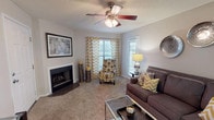 Canter Chase presents a thoughtfully designed single-floor residence that balances comfort and functionality across its key living spaces. The living room serves as the heart of the home, anchored by a classic brick-surround fireplace and outfitted with plush carpeting, a ceiling fan with light fixture, and multiple windows that invite natural light. The open, welcoming layout provides ample room for relaxing and entertaining.

The galley-style kitchen features white cabinetry with brushed nickel hardware, granite-look countertops, hardwood-style flooring, and a full suite of black and stainless steel appliances, including a refrigerator, electric range, and over-the-range microwave. Adjacent to the kitchen, the dining area accommodates a round table beneath a modern multi-pendant chandelier, with convenient in-unit washer access tucked neatly behind bifold doors nearby.

Both bedrooms offer carpeted floors, generous window placements with outdoor views, and a calm, neutral color palette. Each bathroom includes a full tub-shower combination in clean, bright finishes. The overall ambiance of the residence is warm and cohesive, with neutral tones carried consistently throughout, making it a comfortable and move-in-ready living space at Canter Chase.