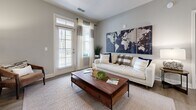 This 2-bedroom, 2-bathroom residence in Augusta, Georgia offers a clean, modern aesthetic with warm neutral tones and wood-look flooring throughout. The open-concept living area is anchored by a bright living room with large windows and a glass-paned door that invites abundant natural light and outdoor views. The kitchen is a standout feature, showcasing light wood cabinetry, granite countertops, stainless steel appliances, pendant lighting, and a spacious island with bar seating — ideal for both cooking and casual dining. A dedicated dining area with a pendant chandelier and an octagonal mirror adds an elegant touch. The primary bedroom is generously sized with plush carpeting, a ceiling fan, and large windows, while the second bedroom offers a similarly comfortable and well-lit retreat. The primary bathroom features a walk-in glass-enclosed shower with tile surround and a modern vanity with ample storage. The second bathroom includes a full soaking tub with tiled surround and a matching vanity. A dedicated laundry room with a full-size washer and dryer provides added convenience. Throughout the residence, soft gray walls, modern fixtures, and consistent finishes create a cohesive and inviting atmosphere.