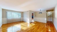 This single-story home offers a well-organized layout comprising four bedrooms, two bathrooms, a kitchen, and a connecting hallway. The living area is immediately welcoming, featuring gleaming hardwood floors that reflect generous natural light streaming through large windows fitted with vertical blinds. A two-tone wall treatment with a white chair rail adds a classic architectural detail, while a stylish pendant light fixture serves as a focal point overhead. The space flows seamlessly toward the kitchen, which is equipped with warm wood cabinetry, dark green granite countertops, a mosaic tile backsplash, a gas range, and classic black-and-white tile flooring. A window above the counter brings in additional natural light and outdoor views.

The four bedrooms continue the hardwood flooring theme and maintain a clean, neutral palette with white walls. Each room receives natural light through windows overlooking outdoor greenery. The primary bedroom is notably spacious, offering ample room for furnishings. Both bathrooms are finished in neutral tones; one features white subway tile with contrasting dark mosaic accents and a tub-shower combination with a sliding frosted glass door. Throughout, the home maintains a consistent, clean aesthetic with practical finishes.