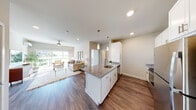This single-floor residence is designed with a modern, open-concept layout that seamlessly connects the kitchen, dining, and living areas. The kitchen is anchored by a central island with granite countertops, an undermount sink, and white cabinetry, complemented by stainless steel appliances including a range and over-the-range microwave. Wood-look flooring extends throughout the main living area, adding warmth and continuity.

The living room is bright and inviting, benefiting from large sliding glass doors that frame outdoor views and flood the space with natural light. A ceiling fan overhead and neutral wall tones contribute to a relaxed, comfortable atmosphere.

The bedroom features plush carpeting, a wall-mounted mini-split unit for climate control, and windows fitted with blinds that allow adjustable natural light. A secondary carpeted room, also equipped with a ceiling fan and a wall-mounted unit, offers flexible use as a den, office, or dining area with its own outdoor-facing window.

Two bathrooms mirror each other in style, each featuring granite-topped vanities with undermount sinks, wood-look flooring, and shower-tub combinations. The overall design palette throughout the residence is neutral and cohesive, creating a clean, contemporary living environment.