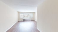 Located at 8608 Skokie Blvd in Skokie, Illinois, this single-floor unit offers a clean, straightforward layout with a bright and neutral aesthetic throughout. Warm-toned hardwood-style flooring runs continuously through the main living areas, lending a cohesive and polished look to the space.

The living area is generously proportioned, featuring cream-colored walls, crisp white baseboards, and a wide window that allows natural light to filter in, offering views of surrounding trees. A wall-unit air conditioner and baseboard radiator provide year-round climate control. The open sightlines through the corridor connect the living space to the rest of the unit, creating a sense of flow and depth.

The kitchen is a functional highlight, outfitted with light maple cabinetry, dark granite countertops, and a striking mosaic glass tile backsplash. Stainless steel appliances — including a gas range with oven, over-the-range microwave, and refrigerator — complement the black dishwasher for a well-equipped cooking space.

The bathroom features classic black-and-white mosaic floor tile, a white vanity with medicine cabinet, and a tub-shower combination, all finished in a clean, timeless style. Additional hardwood-style flooring continues into the bedroom, which includes its own window and climate control unit, completing this well-appointed unit.