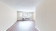 Located at 8608 Skokie Blvd in Skokie, Illinois, this single-floor unit offers a clean, straightforward layout with a bright and neutral aesthetic throughout. Warm-toned hardwood-style flooring runs continuously through the main living areas, lending a cohesive and polished look to the space.

The living area is generously proportioned, featuring cream-colored walls, crisp white baseboards, and a wide window that allows natural light to filter in, offering views of surrounding trees. A wall-unit air conditioner and baseboard radiator provide year-round climate control. The open sightlines through the corridor connect the living space to the rest of the unit, creating a sense of flow and depth.

The kitchen is a functional highlight, outfitted with light maple cabinetry, dark granite countertops, and a striking mosaic glass tile backsplash. Stainless steel appliances — including a gas range with oven, over-the-range microwave, and refrigerator — complement the black dishwasher for a well-equipped cooking space.

The bathroom features classic black-and-white mosaic floor tile, a white vanity with medicine cabinet, and a tub-shower combination, all finished in a clean, timeless style. Additional hardwood-style flooring continues into the bedroom, which includes its own window and climate control unit, completing this well-appointed unit.