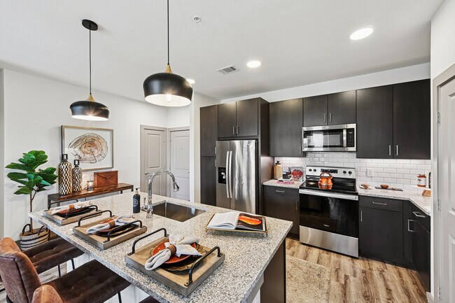 Cocina con gabinetes color espresso, encimeras de granito moteado, protector contra salpicaduras de azulejos blancos tipo metro, electrodomésticos de acero inoxidable y pisos de superficie dura. - Avalon Benbrook