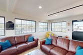 Located at 47 Eagle St in Providence, Rhode Island, this generously sized single-floor space offers a well-appointed layout designed for both comfort and functionality. The living area is bright and welcoming, featuring large multi-pane windows that flood the room with natural light and offer views of the surrounding neighborhood. Rich leather sofas accented with teal throw pillows, tile flooring, and industrial-style black track lighting overhead lend the space a contemporary yet comfortable character. A bar-height counter with seating connects the living area to the kitchen, which is equipped with stainless steel appliances, granite countertops, white cabinetry, and a pass-through window. The vibrant dining room stands out with bold mustard-yellow walls, a round wooden dining table, and large windows framing city views—artwork on the walls adds a creative touch. The accessible bathroom is clean and practical, featuring granite countertops, grab bars, and tile flooring consistent with the rest of the space. An attached outdoor deck area, visible in the floor plan, provides additional space for relaxation with lounge seating. Throughout, the space maintains a cohesive, modern aesthetic with tile flooring, recessed lighting, and an abundance of natural light.