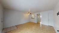 This single-floor home offers a clean, functional layout with a bright and open feel throughout. The spacious living area serves as the heart of the home, finished with warm-toned tile flooring and ceiling fan lighting. Large windows along the front of the space invite an abundance of natural light, creating an airy atmosphere. A second living or flex space connects seamlessly, maintaining the same light tile flooring and ceiling fan, making it ideal for a variety of uses.

The kitchen is efficiently designed with warm wood cabinetry, a granite-style countertop, a double sink, and a range with oven. A pass-through counter with a raised bar connects the kitchen to the living area, enhancing the open-concept feel and making the space well-suited for entertaining.

The bedroom features plush carpet flooring, a ceiling fan, and a window with blinds that allows natural light to filter in while maintaining privacy. The bathroom is tidy and functional, featuring a single vanity with a large mirror, tile flooring, and a neutral color palette throughout.

Overall, the home presents a cohesive, light-filled interior with consistent white walls, tile and carpet flooring, and practical ceiling fans in key rooms — offering a comfortable and move-in ready living environment.