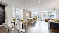 Located at 5350 Burnet Rd in Austin, Texas, this stylish single-floor space seamlessly blends a living lounge and kitchen area into one open, well-appointed layout. The design is unmistakably contemporary, anchored by striking herringbone-patterned flooring that runs throughout and crisp white ceilings equipped with recessed lighting and elegant pendant fixtures.

Floor-to-ceiling windows and full-length glass walls flood the interior with abundant natural light while offering views of an adjacent outdoor patio area, creating a bright and airy atmosphere. Large glass-panel doors provide direct access to the exterior, reinforcing the strong indoor-outdoor connection.

The kitchen counter area features a sleek white bar surface lined with vibrant yellow and teal upholstered bar stools, adding a bold pop of color against the neutral taupe and white walls. A cozy lounge section is anchored by a statement sputnik chandelier overhead, complemented by plush velvet sofas in deep charcoal and grey tones accented with mustard and orange throw pillows. Abstract wall art and geometric wall details add a curated, artistic touch throughout.

A co-working nook with desktop computers is also integrated into the space, alongside glass walls overlooking a well-equipped fitness area. The overall ambiance is polished, welcoming, and energetic — ideal for both relaxing and gathering.