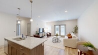 Located at 267 Seminole Rd in Norton Shores, Michigan, this well-appointed 2-bedroom, 2-bathroom single-floor residence offers a thoughtfully designed layout with modern finishes throughout. The open-concept kitchen and living area serves as the heart of the home, where light wood-tone cabinetry, granite countertops, and a large center island with bar seating create a functional and stylish space. Pendant lighting accents the island, while stainless steel appliances—including a range, microwave, and refrigerator—complete the kitchen. The living area extends naturally from the kitchen, featuring light hardwood-style flooring, recessed lighting, and French doors that invite natural light and provide outdoor access. The two bedrooms are carpeted and comfortably sized, with the primary bedroom offering a generous footprint, a large window with natural light, and ample closet space. The second bedroom also includes its own closet. Two bathrooms serve the home; one features a granite-topped vanity with stylish cabinetry and a shower, while the other is conveniently combined with the laundry area. Four closets throughout the unit provide excellent storage. The neutral color palette and clean architectural lines give the space a bright, contemporary ambiance.