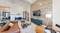 Located at 305 E Hawaii Ave in Nampa, Idaho, this single-floor community clubhouse offers a thoughtfully designed gathering space finished with contemporary style. The grand entrance greets visitors with soaring ceilings, a statement chandelier, warm light wood flooring, and dark-framed glass doors that invite abundant natural light.

The open main area seamlessly blends several functional zones. A comfortable lounge features a dramatic stacked-wood accent wall anchoring a large flat-screen TV, complemented by leather and upholstered seating arranged around a central coffee table. Adjacent, a stylishly appointed social lounge with deep teal accent walls and tall ceilings provides an intimate setting with curated artwork and ample natural light from large windows overlooking the outdoor area.

A central bar-style kitchenette showcases a long white quartz countertop with wood-paneled base, dark cabinetry, pendant lighting, and bar seating — ideal for community gatherings. A secondary kitchen nook provides additional cabinetry, appliances, and prep space.

The dedicated fitness room is carpeted and well-lit, equipped with cardio machines, free weights, a weight bench, a ceiling fan, and full-wall mirrors to maximize the sense of space. Throughout, light hardwood flooring, coffered ceiling details, and cohesive modern-rustic décor create an inviting and functional community environment.
