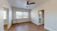 Located in the Koreatown neighborhood of Los Angeles, this single-story unit at 260 S Mariposa Ave offers a well-appointed layout with thoughtful design details throughout. The main living area showcases warm hardwood flooring and a distinctive white-painted exposed brick accent wall, lending the space a blend of character and modern freshness. A ceiling fan with integrated lighting provides both comfort and ambiance, while windows fitted with blinds allow for natural light and privacy control. An en-suite bathroom is conveniently accessible directly from the main room. A separate area of the unit offers additional open living space, also finished with matching hardwood floors and a ceiling fan, with access to a walk-in closet or storage area. The kitchen is well-equipped, featuring slate-blue shaker cabinetry, white subway tile backsplash, clean white countertops, stainless steel appliances including a refrigerator and gas range, and a built-in range hood. The bathroom is stylishly appointed with floor-to-ceiling dark marble-effect tile, a soaking bathtub with chrome fixtures, a white vanity with sink, a lighted mirror, and a window that brings in natural light. The unit's cohesive design, combining classic architectural elements with modern finishes, creates a comfortable and inviting living environment.