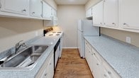 This single-floor, one-bedroom, one-bathroom unit offers a practical and comfortable layout designed to maximize its well-proportioned footprint. Throughout the main living areas and bedroom, warm-toned hardwood-style flooring creates a cohesive and inviting atmosphere, complemented by neutral beige walls and clean white baseboards.

The open living area features recessed lighting, a window with horizontal blinds allowing natural light, and direct access to the entry door. The space flows seamlessly toward the kitchen and bedroom, as visible in the unit's layout. The galley-style kitchen is efficiently designed with white cabinetry lining both walls, speckled laminate countertops, a stainless steel sink, and white appliances including a range, built-in microwave, dishwasher, and refrigerator, all set atop hardwood-style flooring.

The bedroom is well-appointed, featuring a ceiling fan with light fixture, a sliding glass door with blinds providing outdoor views and natural light, and notable dual closets offering generous storage. A door with a full-length mirror adds functionality.

The bathroom includes a full tub-shower combination with white tile surround, a toilet, a vanity with speckled countertop, an over-toilet storage cabinet, and a mirror, completing the unit's practical design.