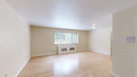 Located at 5530 5th Ave in Pittsburgh's Shadyside neighborhood, this two-bedroom, one-bathroom unit offers a practical and well-laid-out single-floor living space. The living room is the largest area of the home, featuring light-toned hardwood flooring that reflects natural light from a wide front-facing window fitted with blinds. A classic radiator enclosure beneath the window adds a charming architectural touch. The kitchen is efficiently designed with light wood cabinetry, stainless steel countertops, a gas range, dishwasher, and a window providing natural ventilation. The tile flooring adds a clean, functional finish. Both bedrooms are carpeted and feature windows overlooking greenery, with radiators providing supplemental heating. The primary bedroom benefits from direct access to the bathroom and includes a closet. The second bedroom features a vintage cast-iron radiator and a window unit for cooling. The hallway connects all rooms in a logical flow. The bathroom is a standout with retro charm — pink ceramic wall tiles accented by black borders, hexagonal mosaic floor tiles, a pedestal sink, a soaking tub, and art deco-style vanity lighting complete this characterful space.