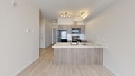 Located at 15 Broadway Rise in Sylvan Lake, Alberta, this well-designed one-bedroom, one-bathroom unit offers a thoughtful and efficient layout spread across a single floor. Light hardwood-style flooring flows throughout the space, complementing the clean white walls and creating a bright, cohesive aesthetic.

The open-concept kitchen, dining, and living area serves as the heart of the unit. The kitchen is outfitted with warm wood-toned cabinetry, a white tile backsplash, stainless steel appliances including a range and over-the-range microwave, a full-size refrigerator, and a peninsula with a light stone countertop and integrated sink — ideal for both cooking and casual dining. Track lighting above adds a contemporary touch.

The primary bedroom is a comfortable, well-proportioned room filled with natural light from a dedicated window. It includes a closet, providing practical storage. An additional closet and a flexible den offer further versatility for storage or a home office setup.

The bathroom features a tub-shower combination with white tile surround, a wood-toned vanity with a stone-look countertop, and a large mirror. In-suite laundry adds everyday convenience. A hallway connects the rooms seamlessly, contributing to the unit's efficient and livable flow.