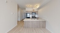Located at 15 Broadway Rise in Sylvan Lake, Alberta, this well-designed one-bedroom, one-bathroom unit offers a thoughtful and efficient layout spread across a single floor. Light hardwood-style flooring flows throughout the space, complementing the clean white walls and creating a bright, cohesive aesthetic.

The open-concept kitchen, dining, and living area serves as the heart of the unit. The kitchen is outfitted with warm wood-toned cabinetry, a white tile backsplash, stainless steel appliances including a range and over-the-range microwave, a full-size refrigerator, and a peninsula with a light stone countertop and integrated sink — ideal for both cooking and casual dining. Track lighting above adds a contemporary touch.

The primary bedroom is a comfortable, well-proportioned room filled with natural light from a dedicated window. It includes a closet, providing practical storage. An additional closet and a flexible den offer further versatility for storage or a home office setup.

The bathroom features a tub-shower combination with white tile surround, a wood-toned vanity with a stone-look countertop, and a large mirror. In-suite laundry adds everyday convenience. A hallway connects the rooms seamlessly, contributing to the unit's efficient and livable flow.