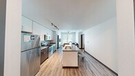 Located in Austin, TX (78705), this modern 3-bedroom, 4-bathroom unit offers a thoughtfully designed open-concept layout across a single floor. The kitchen and living area flow seamlessly together, anchored by a central island with a quartz countertop and stainless steel sink — ideal for both meal prep and casual dining. The kitchen is equipped with stainless steel appliances, including a refrigerator, electric range, and built-in microwave, complemented by dual-tone cabinetry featuring white uppers and dark wood lowers. Track lighting illuminates the workspace effectively. Light wood-style flooring runs throughout the common areas, adding warmth to the contemporary palette. The living room benefits from large windows fitted with horizontal blinds, allowing ample natural light, and is finished with an exposed concrete ceiling and a ceiling fan. Each of the three bedrooms is compact yet functional, with built-in closet storage and access to natural light. The four bathrooms are cleanly finished with large-format tile, dark wood vanities with quartz countertops, framed mirrors, and modern fixtures — with at least one featuring a full tub/shower combination. Two hallways connect the private rooms efficiently, maintaining a clean and organized flow throughout the space.