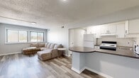 Located at 1412 East St in New Britain, CT, this 2-bedroom, 1-bathroom residence offers a practical and well-appointed single-floor layout. The open-concept living and kitchen area serves as the heart of the home, featuring light-toned laminate wood flooring, neutral gray walls, and a textured ceiling. The kitchen is equipped with white cabinetry, a white refrigerator, an electric range, a dishwasher, and a microwave, centered around a curved peninsula countertop with dark granite-style laminate — ideal for casual dining or meal prep. The living room flows seamlessly from the kitchen and is brightened by large windows with horizontal blinds that frame views of the surrounding neighborhood. The spacious primary bedroom includes a sliding-door closet with built-in shelving and access to an in-unit laundry area. The second bedroom is well-sized with its own window and closet. The bathroom features a full soaking tub with a shower and clean white surround. Throughout the unit, consistent flooring, ample natural light, and a cohesive neutral color palette create a clean, functional living environment.