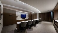 Located at 40 Pinehills in Plymouth, MA, this elegantly designed single-floor space serves as both a professional meeting room and a comfortable lounge area. The interior is defined by a cohesive, upscale aesthetic that combines warm dark-wood wall paneling with neutral carpeting and a carefully layered lighting scheme featuring recessed ceiling lights and a distinctive curved cove detail that adds architectural depth overhead.

The primary focal point of the room is a striking media wall clad in light stone tile, housing a large flat-screen display above a dark wood credenza with ample cabinetry. Flanking the media wall, dark wood paneling extends across the full width, providing a rich, grounded backdrop. A long marble-topped conference table with patterned upholstered swivel chairs accommodates multiple attendees for meetings or presentations.

A dedicated lounge area offers a comfortable arrangement of cream leather armchairs and a round ottoman, ideal for informal gatherings or relaxed discussions. Framed artwork decorates the walls, adding a curated, hospitality-inspired feel. Floor-to-ceiling drapes in warm taupe soften the space and allow for light control. A short staircase with a handrail connects to an adjacent entry or anteroom, completing the functional layout of this refined, well-appointed space.