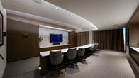 Located at 40 Pinehills in Plymouth, MA, this elegantly designed single-floor space serves as both a professional meeting room and a comfortable lounge area. The interior is defined by a cohesive, upscale aesthetic that combines warm dark-wood wall paneling with neutral carpeting and a carefully layered lighting scheme featuring recessed ceiling lights and a distinctive curved cove detail that adds architectural depth overhead.

The primary focal point of the room is a striking media wall clad in light stone tile, housing a large flat-screen display above a dark wood credenza with ample cabinetry. Flanking the media wall, dark wood paneling extends across the full width, providing a rich, grounded backdrop. A long marble-topped conference table with patterned upholstered swivel chairs accommodates multiple attendees for meetings or presentations.

A dedicated lounge area offers a comfortable arrangement of cream leather armchairs and a round ottoman, ideal for informal gatherings or relaxed discussions. Framed artwork decorates the walls, adding a curated, hospitality-inspired feel. Floor-to-ceiling drapes in warm taupe soften the space and allow for light control. A short staircase with a handrail connects to an adjacent entry or anteroom, completing the functional layout of this refined, well-appointed space.