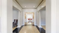 Located at 4700 City Ave in Philadelphia, PA, this generously proportioned single-floor space commands attention with its refined classical architectural design. The grand entrance is defined by stately decorative columns, polished marble tile flooring in contrasting tones, and tray ceilings with recessed lighting, setting an elegant tone throughout.

Multiple living areas offer versatile and comfortable gathering spaces, each featuring hardwood floors, crown molding, and an abundance of natural light streaming through large multi-pane windows. A distinctive bay-windowed sitting room provides sweeping outdoor views and is complemented by a cozy lounge nook with built-in cabinetry — ideal as a beverage station or kitchenette.

The formal dining room exudes sophistication with warm taupe walls, sheer-draped windows, rich hardwood floors layered with a patterned area rug, and a bold pendant chandelier above a long dining table.

The gourmet kitchen is a standout, featuring deep navy cabinetry, dark granite countertops, a striking ornately carved range hood with subway tile surround, stainless steel appliances including double wall ovens, and a large marble-topped island. Throughout, the space is unified by consistent millwork detailing, crown molding, and a polished, welcoming ambiance.