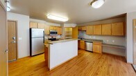 Located at 1910 35th Ave SW in Minot, North Dakota, this single-floor unit offers a practical and comfortable layout designed for everyday living. The kitchen serves as a functional centerpiece, featuring warm honey-toned cabinetry, stainless steel appliances including a refrigerator, range, microwave, and dishwasher, durable laminate countertops, a double-basin sink, and a central island for additional prep space. A dedicated pantry with wire shelving provides generous storage. The kitchen flows seamlessly onto easy-care hardwood-style flooring that extends throughout the main living areas. The bedrooms are carpeted for comfort and each includes a ceiling fan with light, a window with blinds allowing natural light, and baseboard heating. Two bathrooms serve the unit: one features a full tub-shower combo, a vanity, and tile flooring, while the second offers a dual-sink vanity with a large mirror and matching tile flooring. A dedicated laundry room houses a full-sized washer and dryer with overhead shelving, adding significant convenience. The unit's neutral color palette, warm wood trim, and consistent finishes throughout create a cohesive and welcoming atmosphere.