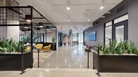 The Station is a thoughtfully designed single-floor commercial lobby space offering a generous footprint that balances open circulation with distinct functional zones. The interior is anchored by polished concrete floors that extend throughout, reflecting the recessed and track lighting overhead and contributing to a clean, contemporary aesthetic.

The design blends industrial and modern elements seamlessly. Exposed structural columns, visible overhead ductwork and conduit, and a bold black steel grid canopy define key gathering areas while adding architectural character. Beneath the grid canopy, a lounge area features vibrant yellow, blue, and white upholstered seating arranged atop a colorful patterned area rug, offering a warm contrast to the otherwise neutral palette.

A dedicated mailroom section houses sleek, dark-paneled parcel and mailbox banks arranged in a well-organized configuration. Adjacent corridors lined with black-framed glass partitions and ribbed glass panels lead to additional rooms and entry points.

Throughout the space, tall planter boxes filled with lush greenery introduce a natural element. Dark slate-blue accent walls, a reception credenza with light wood cabinetry, and a prominent branded "The Station" display board reinforce a polished, welcoming identity across the entire space.