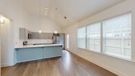 This single-story residence in Warner Robins, Georgia, showcases a thoughtfully designed open-concept layout with striking vaulted ceilings that lend an expansive, airy quality to the main living and kitchen areas. The soaring ceiling height is accentuated by stylish globe pendant lights that hang gracefully over the kitchen island, creating a focal point that blends form and function.

The kitchen is well-appointed with gray shaker-style cabinetry, crisp white countertops, a subway tile backsplash, and a full suite of stainless steel appliances, including a refrigerator, electric range, over-the-range microwave, and dishwasher. A generously sized island with an undermount sink provides additional prep space and seating potential. Wood-look flooring runs throughout the kitchen and living areas, offering both durability and a warm aesthetic.

The living area benefits from abundant natural light through large windows fitted with horizontal blinds, offering views of the surrounding neighborhood. The bedroom features a ceiling fan, dual windows, and the same rich wood-look flooring. The bathroom is clean and functional, with gray vanity cabinetry, white countertops, a tub-shower combination, and coordinating wood-look flooring, maintaining a consistent modern palette throughout the home.