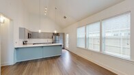 This single-story residence in Warner Robins, Georgia, showcases a thoughtfully designed open-concept layout with striking vaulted ceilings that lend an expansive, airy quality to the main living and kitchen areas. The soaring ceiling height is accentuated by stylish globe pendant lights that hang gracefully over the kitchen island, creating a focal point that blends form and function.

The kitchen is well-appointed with gray shaker-style cabinetry, crisp white countertops, a subway tile backsplash, and a full suite of stainless steel appliances, including a refrigerator, electric range, over-the-range microwave, and dishwasher. A generously sized island with an undermount sink provides additional prep space and seating potential. Wood-look flooring runs throughout the kitchen and living areas, offering both durability and a warm aesthetic.

The living area benefits from abundant natural light through large windows fitted with horizontal blinds, offering views of the surrounding neighborhood. The bedroom features a ceiling fan, dual windows, and the same rich wood-look flooring. The bathroom is clean and functional, with gray vanity cabinetry, white countertops, a tub-shower combination, and coordinating wood-look flooring, maintaining a consistent modern palette throughout the home.