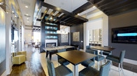 Located at 11775 Wadsworth Boulevard in Broomfield, Colorado, this single-floor amenity space delivers a polished, contemporary atmosphere designed for social gathering and recreation. The interior is defined by a striking coffered ceiling with dark exposed beams and geometric detailing, creating a dramatic overhead focal point that draws the eye upward. Pendant lighting hangs gracefully above, complementing the high-contrast design palette of deep charcoal, warm white, and teal accents.

A full-size billiards table anchors the central recreation area, surrounded by stylish upholstered seating in a coordinating teal and charcoal pattern. High-top tables and bar-height chairs are arranged nearby, offering comfortable spots for casual conversation or social activities. A sleek fireplace set into a dark accent wall adds warmth and a refined visual centerpiece to the lounge area.

Built-in display niches with teal backlighting provide decorative depth along the accent wall, while framed artwork adds a curated, gallery-like quality to the space. An adjacent area, visible through an open sightline, features additional bar seating and lighting, suggesting a seamlessly connected dining or entertainment zone. The tile flooring throughout ties the various areas together, reinforcing the space's clean, modern aesthetic.