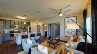 Located in Jacksonville, FL (32224), this single-story residence offers a thoughtfully designed open-concept floor plan that seamlessly connects the kitchen, dining, and living areas. The kitchen is a standout feature, showcasing a large granite-topped island with an undermount sink, pendant lighting, dark wood cabinetry, and a full suite of stainless steel appliances including a refrigerator, range, and microwave. The living area is generously proportioned, bathed in natural light from large windows and French doors that open to an outdoor balcony, offering views of the surrounding landscape. A ceiling fan adds comfort and visual interest overhead. The space includes two well-sized bedrooms, each carpeted and outfitted with ceiling fans and windows that bring in ample natural light. The bathroom features dark wood vanity cabinetry with granite countertops, wood-look flooring, and a walk-in glass-enclosed shower. Wood-look flooring extends throughout the main living areas, adding warmth and continuity. A dedicated in-unit laundry area with washer and dryer hookups adds everyday convenience. The overall aesthetic is modern and cohesive, with neutral tones, gray accents, and contemporary finishes throughout.
