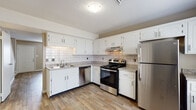 This two-floor residence is laid out to provide a clear distinction between living and sleeping areas. The main level features wood-look plank flooring that flows through the open living area and into the kitchen. A carpeted staircase with white railings connects the floors, and the entryway leads directly into the main living space, which benefits from a straightforward, functional layout.

The kitchen is a notable feature of the main level, equipped with white raised-panel cabinetry, granite-patterned countertops, and a white subway tile backsplash. Stainless steel appliances — including a refrigerator, range, and dishwasher — are integrated into the L-shaped layout, complemented by an under-cabinet range hood and a double-basin stainless steel sink.

The upper level hosts the bedrooms, each finished with neutral-toned carpet and featuring windows fitted with horizontal blinds that allow natural light while maintaining privacy. The walls throughout are painted in warm neutral tones, contributing to a cohesive, understated atmosphere. A full bathroom on the upper level includes a tub-shower combination with a clean white surround, wood-look flooring, and a white vanity. Textured ceilings are present throughout the home.