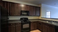 Located at 5806 Ogeechee Rd in Savannah, Georgia, this single-story space offers a comfortable and functional layout designed with practicality in mind. The kitchen serves as a standout feature, showcasing rich, dark espresso-toned cabinetry that extends from floor to ceiling, providing ample storage throughout. Dark granite-style countertops complement the cabinetry, creating a cohesive and polished aesthetic. Black appliances, including an electric range and an over-the-range microwave, are seamlessly integrated into the kitchen design. Light hardwood-style flooring runs through the space, offering a warm contrast to the darker cabinetry and countertops. Crown molding along the ceiling adds a refined architectural detail, contributing to an elevated finish throughout. The walls feature a soft, neutral tone that enhances the brightness of the space and pairs well with the bold cabinetry. The overall ambiance of this Savannah property is one of understated elegance, blending functional design with quality finishes to create an inviting and well-organized environment suitable for everyday living or professional use.