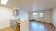 This single-floor, one-bedroom, one-bathroom unit offers a well-organized layout that maximizes its compact footprint. Light hardwood-style flooring runs throughout the space, contributing to a clean and cohesive aesthetic.

The combined kitchen and living area forms the heart of the unit. The galley-style kitchen is equipped with stainless steel appliances, including a refrigerator, range, microwave, and dishwasher, complemented by gray cabinetry and granite-style countertops. A peninsula with a stainless steel sink separates the kitchen from the living area, creating an open, functional flow. The living space receives natural light through a window and glass-paneled entry door, with a wall-mounted HVAC unit providing climate control.

The bedroom is a well-proportioned, private room featuring a window with an outdoor view and a baseboard heater. Its neutral wall tones and light flooring create a calm atmosphere.

The bathroom includes a full tub-shower combination, a toilet, and a vanity with gray cabinetry and a granite-style countertop, maintaining the consistent design language found throughout the unit. Textured ceilings are present in the main living areas.