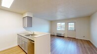 This single-floor, one-bedroom, one-bathroom unit offers a well-organized layout that maximizes its compact footprint. Light hardwood-style flooring runs throughout the space, contributing to a clean and cohesive aesthetic.

The combined kitchen and living area forms the heart of the unit. The galley-style kitchen is equipped with stainless steel appliances, including a refrigerator, range, microwave, and dishwasher, complemented by gray cabinetry and granite-style countertops. A peninsula with a stainless steel sink separates the kitchen from the living area, creating an open, functional flow. The living space receives natural light through a window and glass-paneled entry door, with a wall-mounted HVAC unit providing climate control.

The bedroom is a well-proportioned, private room featuring a window with an outdoor view and a baseboard heater. Its neutral wall tones and light flooring create a calm atmosphere.

The bathroom includes a full tub-shower combination, a toilet, and a vanity with gray cabinetry and a granite-style countertop, maintaining the consistent design language found throughout the unit. Textured ceilings are present in the main living areas.