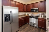 Located at 180 Waterview Dr in Oak Ridge, Tennessee, this single-floor residence offers a well-organized layout designed for comfortable everyday living. The entryway opens into a carpeted hallway that leads directly into the combined dining and kitchen area. The kitchen is equipped with rich, dark cherry wood cabinetry, granite-style countertops, hardwood-style flooring, and a full suite of stainless steel appliances including a gas range, over-the-range microwave, and a French door refrigerator with an ice and water dispenser. The adjacent dining area comfortably seats four and flows seamlessly into the rest of the living space. Crown molding accents the ceiling of the living room, which features soft carpeting, a ceiling fan with light fixture, and French doors that open to a private outdoor balcony, allowing for natural light and outdoor access. The residence includes multiple bedrooms, each finished with plush carpeting and neutral toned walls. One bedroom features a large window with blinds providing ample natural light, while another includes a louvered closet. The two full bathrooms are clean and functional, each featuring a tub-shower combination with white tile surround and brushed nickel fixtures. One bathroom includes hardwood-style flooring and a louvered closet for additional storage.