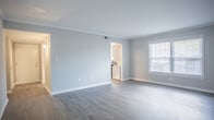 Located at 2100 Criston Dr in Newport News, Virginia, this single-floor residence offers a well-organized layout with a clean, modern aesthetic throughout. The open living area features rich hardwood-style flooring and crown molding, with a large window that allows natural light to fill the space, creating a bright and welcoming atmosphere.

The kitchen is fully equipped with white shaker-style cabinetry, dark countertops, and a full suite of black appliances including a refrigerator, electric range, and dishwasher. A window above the sink provides additional natural light, and a stacked washer and dryer unit is conveniently integrated into the kitchen area, adding practical in-unit laundry access.

The bedrooms are carpeted for comfort and feature neutral walls and generous closet space. The primary bedroom includes dual closets, offering substantial storage. Additional bedrooms are well-proportioned, each with their own closet and windows that bring in natural light.

The bathroom is finished with white tile wainscoting, a single vanity with a large mirror, and a shower-tub combination. The overall design of the space is functional and tastefully neutral, making it move-in ready and easy to personalize.