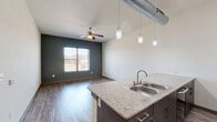 Located at 612 E Hickory St in Denton, TX, this one-bedroom, one-bathroom unit offers a well-designed layout across a single floor. The open-concept kitchen and living area serves as the heart of the space, highlighted by a large granite-topped island with a double stainless steel sink and pendant lighting suspended from exposed industrial-style ductwork. The kitchen is equipped with stainless steel appliances, including a refrigerator and microwave, complemented by a gas range, a tile backsplash, and white upper cabinetry. Wood-style plank flooring runs throughout the main living area, which features a ceiling fan, a bold dark accent wall, and a window that invites natural light. The bedroom is a comfortable retreat with plush carpeting, a ceiling fan, and a window offering views of the surrounding area. A dedicated closet provides ample storage. The bathroom is finished with large-format gray tile surrounding a soaking tub and shower combination, a granite vanity, and dark wood cabinetry. A hallway connects the rooms efficiently, completing the functional and modern layout of this Denton residence.